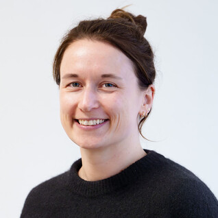 Portrait einer Frau mit hochgesteckten dunklen Haaren und hellem Pullover.